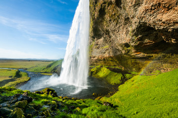 Seljalandsfoss waterfall in sunny day with green grass around