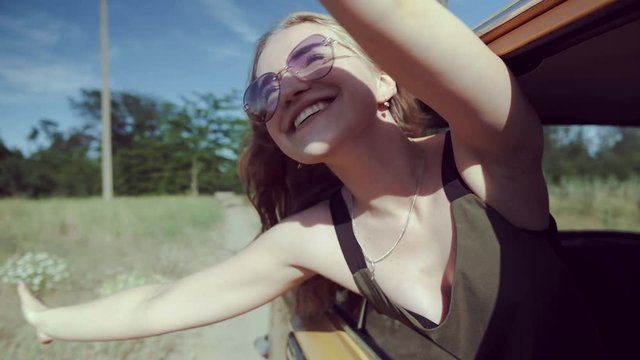A happy young woman leans out of the car window at high speed, her hair is intertwined in the wind, she laughs and enjoys the oncoming airflow in anticipation of a happy vacation trip.