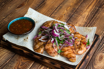 Grilled meat with onion and sauce on a wooden table.	