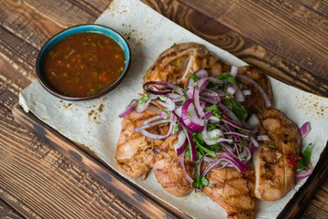 Grilled meat with onion and sauce on a wooden table.	