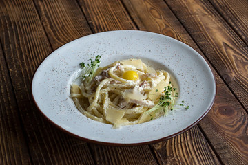 Pasta with parmesan, basil, and becon on a wooden table. Pasta carbonara.