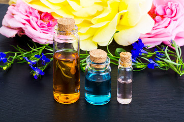 Three bottles of essential oil with fresh  flowers on black background