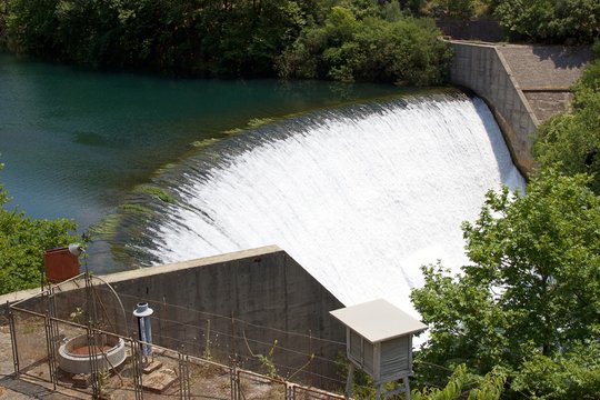 Water spills over the top of Louros river hydroelectric dam and power station in a green forest in Epirus Greece, near the town of Filippiada 