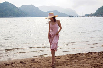 girl in straw hat and pink dress walking on the beach