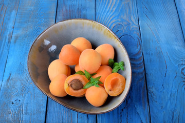 Ripe apricots in a ceramic bowl on the blue table