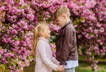 Kids in love pink cherry blossom. Love is in the air. Couple adorable lovely kids walk sakura garden. Tender love feelings. Little girl and boy. Romantic date in park. Spring time to fall in love