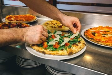 Preparing italian pizza with  Parmigiano cheese  tomato garnished with fresh vegetables and basil and rocket leaves.