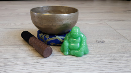 Hand singing bowl and Buddha statuette are on the wooden floor.