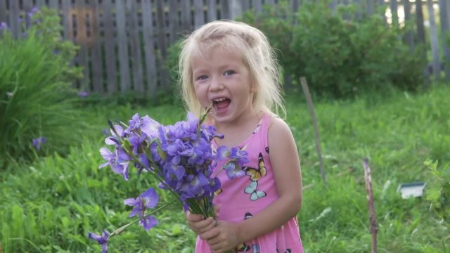 The little girl laughs with a bouquet of flowers in her hands. Summer farm