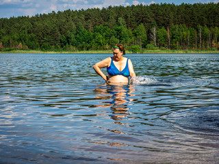 Mature woman in blue swimsuit comes out of the water