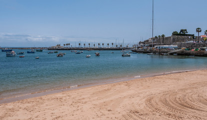 Beautiful empty beach in Cascais, Portugal showing the traditional architecture and fishing boats off the coast. Taken on a sunny summer day.