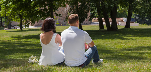 The happy young couple on an appointment in the city park sits on a grass, enjoy the beautiful nature