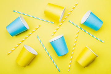 Blue and yellow paper cups and straw on blue background. Top view