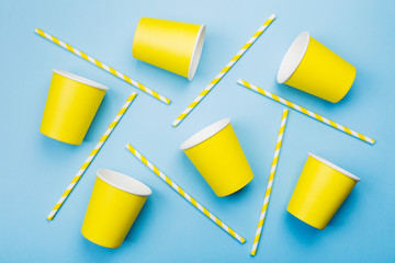 Yellow paper cups and yellow-white straw on blue background. Top view