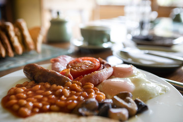traditional British and Scottish breakfast with egg, beans, tomato, mushroom and haggis served on a white plate, standing on a table with a blurred background