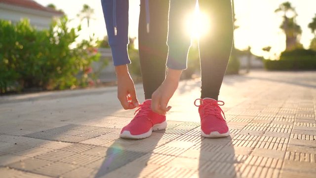 Close up of woman tying shoe laces and running along the palm avenue at sunset. Slow motion