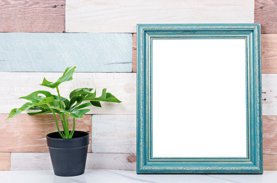 Blank vintage photo frame on wooden wall with plant.
