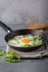 Green shakshuka. Fried eggs with fresh pepper, beans on a gray background, rustic style
