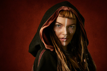 Attractive, young, stylish woman in a black, tribal hood on red background