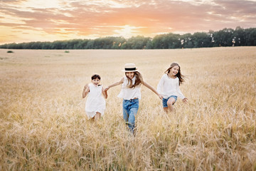 Naklejka premium Group of three smiling girls running in the wheat field at sunset