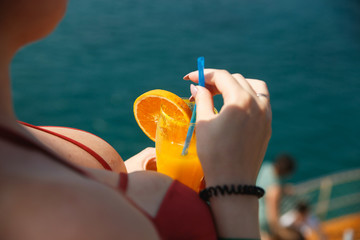 Sexy busty woman on yacht. Lady in girl in coral bra holding fresh orange drink. Cool drink and fresh aquamarine sea. Living a happy life.