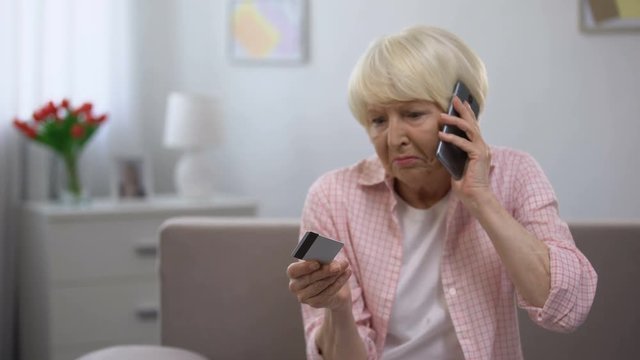 Confused aged woman with credit card calling bank support, payment problems
