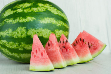 A big juicy ripe green watermelon lies on a white wooden table with chopped red pieces. Concept of...