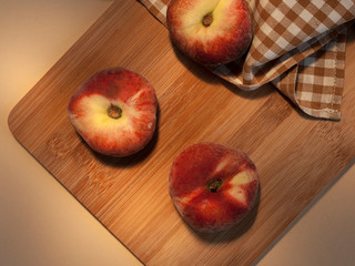Three peaches on a wooden board with an orange checkered napkin on a background.