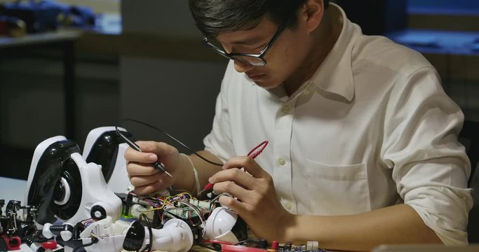 Young asian electronics development engineers building, testing, fixing robotics in computer science research laboratory at night. People with technology or innovation concept.