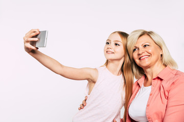 Selfie with grandma! Family holidays and celebrations. Close up photo of happy grandmother and granddaughter in good and fun mood isolated together on white background.