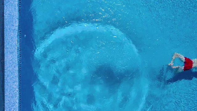 View from the top as a man stands on the edge of the pool, dives and swims under the water
