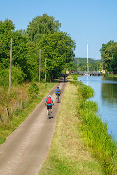 Cyclists cycling on a road by a canal in an idyllic summer landscape