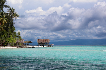 Old wooden platform on stilts over the blue, turquoise ocean with dramatic clouds in the background in Raja Ampat, Papua, Indonesia.