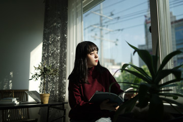 독서 중 창문 밖을 보는 젊은 여성