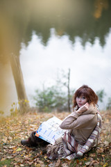 A beautiful brunette girl with curls, autumn in the Park by the water reading a book, clothes beige wool large knit, scarf warm, wind blowing, yellow foliage.