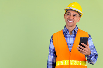 Happy multi ethnic man construction worker thinking while using phone