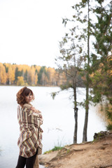 Golden autumn shooting on the lake girl stands back, brunette with curls, wrapped in a warm blanket of light brown. the scarf is knit.