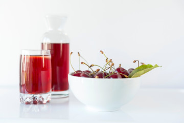 A bowl of cherry with a carafe and a cherry juice on a white background, close up