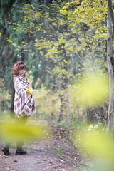 A pregnant woman with a warm blanket and yellow maple leaves walks in the Park, around the beautiful Golden autumn, all brown yellow and gold.