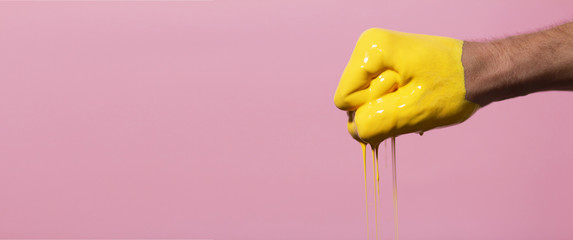 man's hand clenched into a fist smeared in yellow paint on a pink color studio background, a creative idea advertising dye, gesture punch, break through, male positive life style
