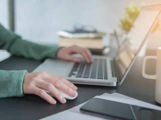 Woman hand use a laptop with wireless mouse on desk at home.