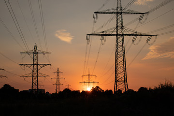 Fototapeta premium Überland Stromleitungen, Hochspannungsmasten im Sonnenuntergang