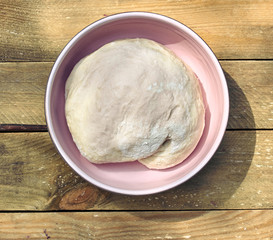 Dough in a pink bowl  on rustic rough wooden table, overhead top view, flat lay, closeup, copy space, homemade cooking and pastery concept