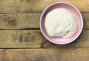 Dough in a pink bowl  on rustic rough wooden table, overhead top view, flat lay, closeup, copy space, cooking bread and pastery concept
