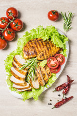 Grilled chicken breasts with salad leaves, cherry tomatoes on white dish. Top view, space for text.
