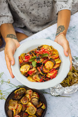 Ratatouille. Woman hands holds traditional homemade French stewed seasonal vegetables dish.  Tomatoes, garlic, onions, zucchini, aubergine (eggplant), bell peppers, marjoram, fennel and basil leaves.