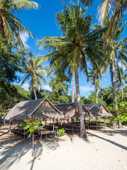 BANANA ISLAND, PHILIPPINES - November 2018: View of wooden houses and palm trees on white sandy beach. Idillyc view for relax and holidays. Travel concept, background