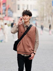 Portrait of a handsome Chinese young man with Korean style clothes walking on street and talking in mobile phone with Shanghai Nanjing road background, male fashion, cool Asian young man lifestyle.