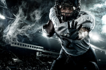 American football player. Sportsman with ball in helmet on stadium in action. Sport wallpaper. Closeup portrait.