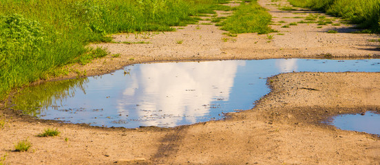Reflection of the cloud in the puddle on a dirt road in sunny weather_